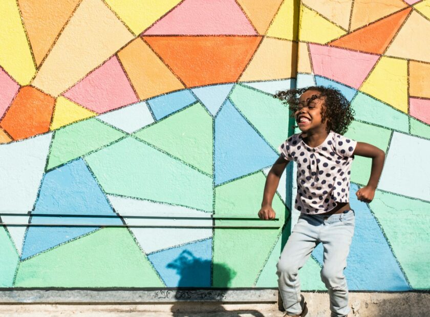 A smiling child jjumping, with a colourful backgrounf behind.