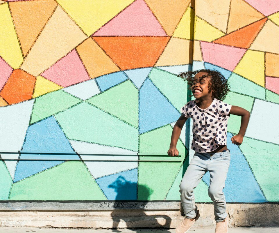 A smiling child jjumping, with a colourful backgrounf behind.